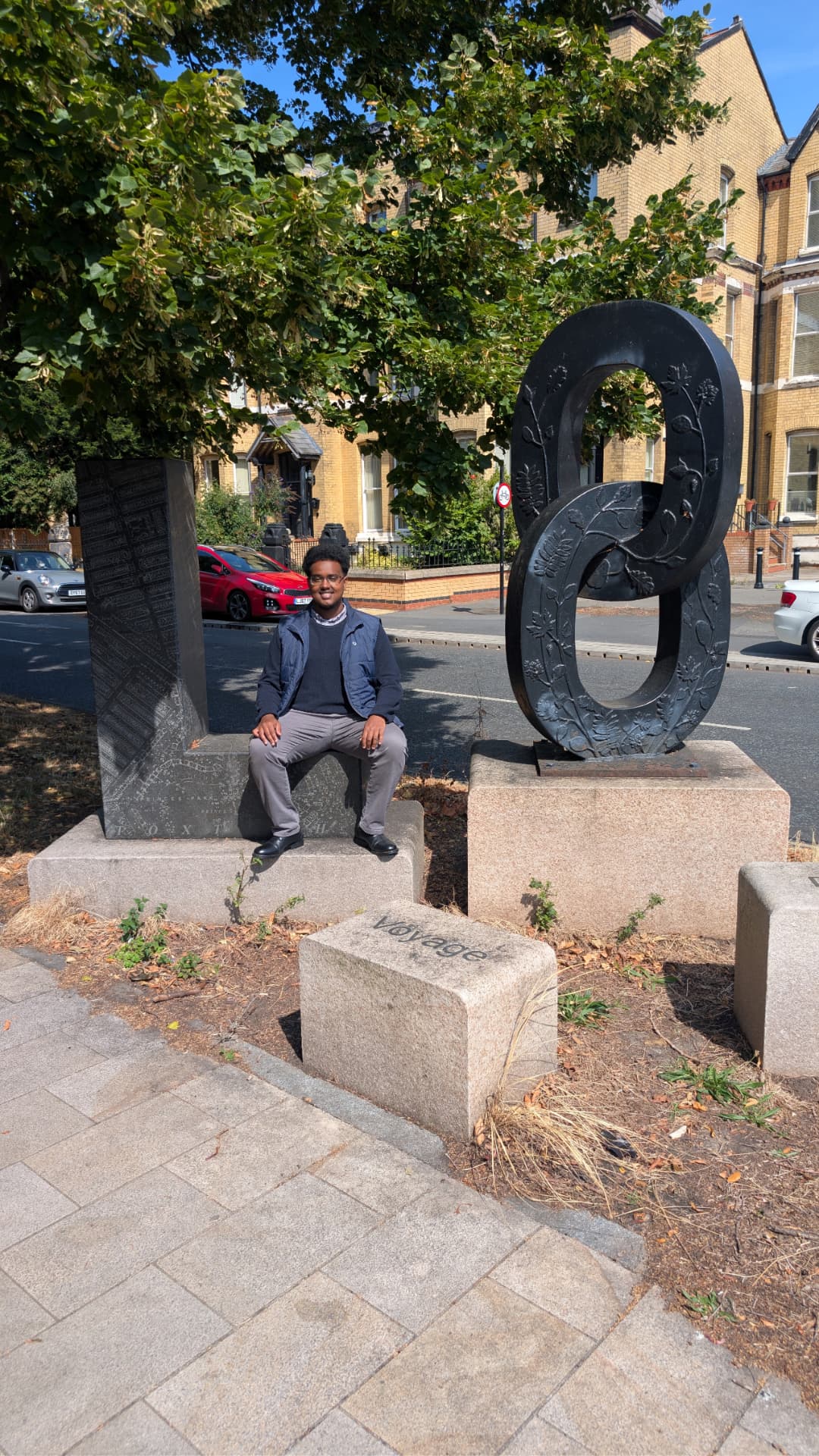 Abdi Ahmed sitting beside the Voyage sculpture on Princes Park Avenue, L8