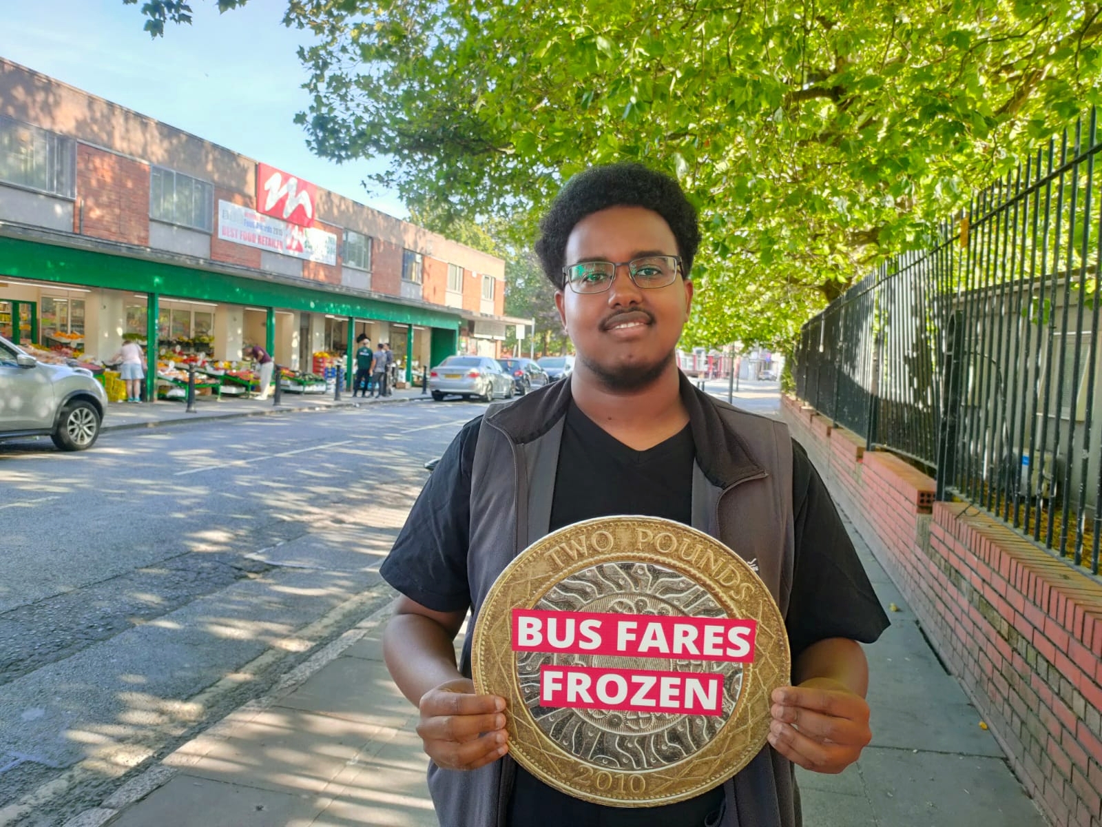 Abdi Ahmed holding a Bus Fares Frozen sign in Princes Park, L8